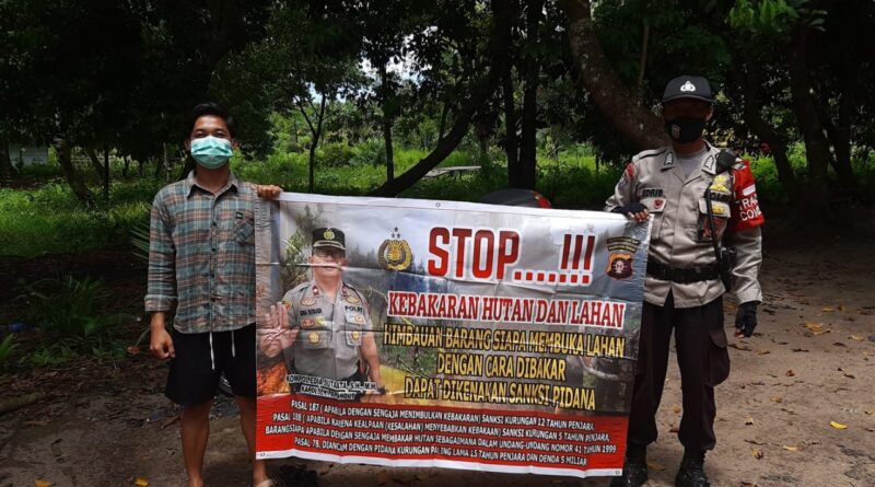 Foto Bripka Mokh Abdullah Edris saat pegang spanduk imbauan Karhutla